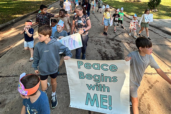  Students hold a sign that reads "Peace Begins with Me" while walking through a neighborhood.